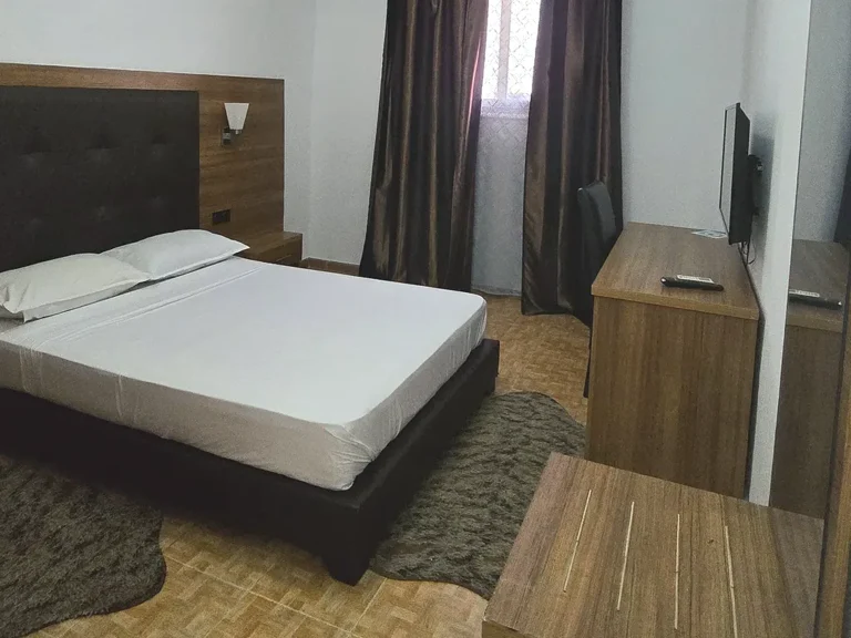Chambre simple avec lit double, tête de lit capitonnée, bureau et télévision